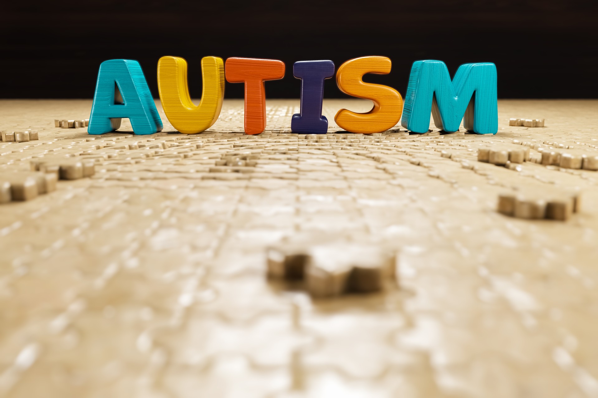 The illustration shows the words autism with copy space in 3D rendering, superimposed over a backdrop made of jigsaw puzzle pieces.